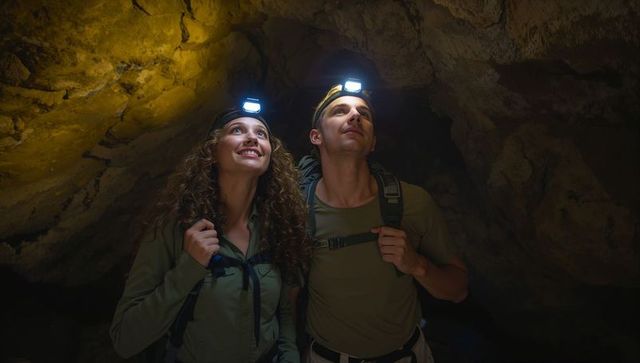 Young couple exploring limestone cave wearing headlamps and backpacks during adventure