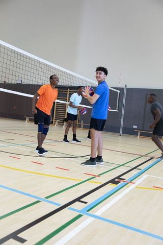Diverse male teammates practicing volleyball in school gym holding balls and preparing serve
