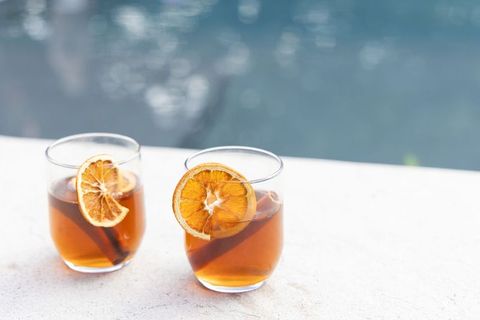 Poolside amber cocktails with dried orange wheels and cinnamon sticks on white ledge