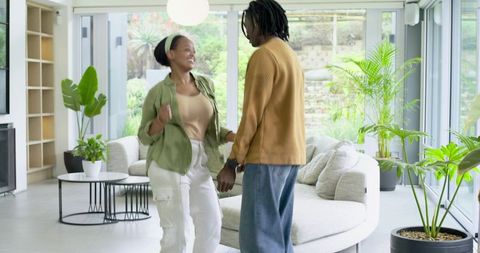 African American couple dancing and smiling in bright modern living room with plants