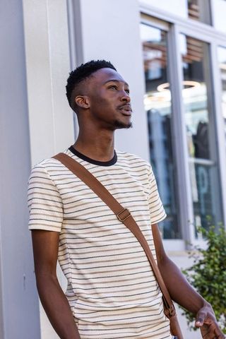 African man standing outdoors wearing striped shirt and crossbody bag looking up