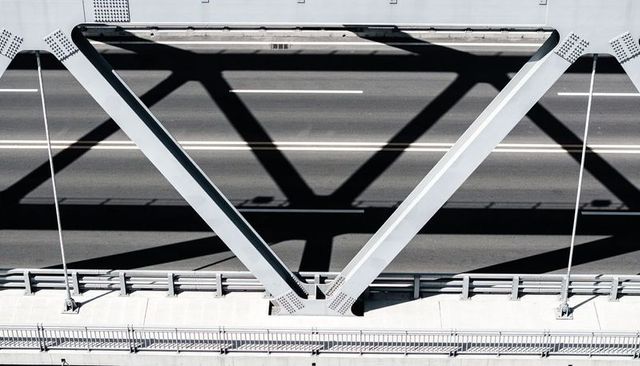 Casting v-shaped steel truss shadows across sunlit urban bridge and roadway