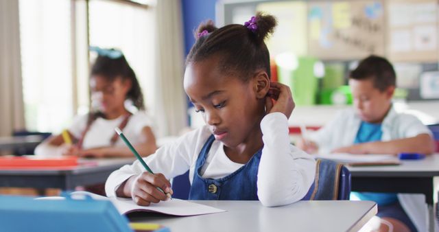 Portrait of african american schoolgirl sitting in classroom, making notes. children at primary school in summer.