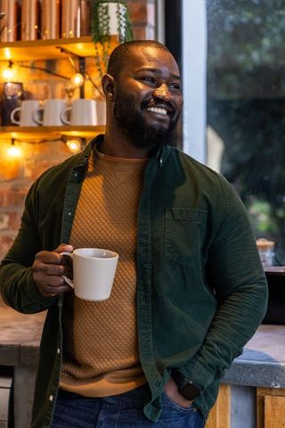 African american man enjoying coffee by window in cozy kitchen with warm string lights