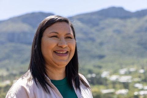 Mature woman smiling on sunlit hillside with mountain valley view