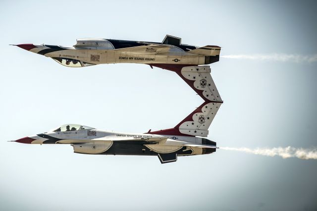 Image featuring two military jets performing a precise aerial maneuver during an airshow with clear sky background. Ideal for use in promotional materials for aviation events, military publications, demonstration flight posters, and educational content on aviation and aerobatics. This image emphasizes the skill of the pilots and the precision of military aircraft in an airshow environment.