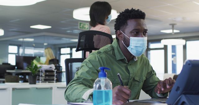 Focused man in office wearing face mask working on tablet - Download Free Stock Images Pikwizard.com