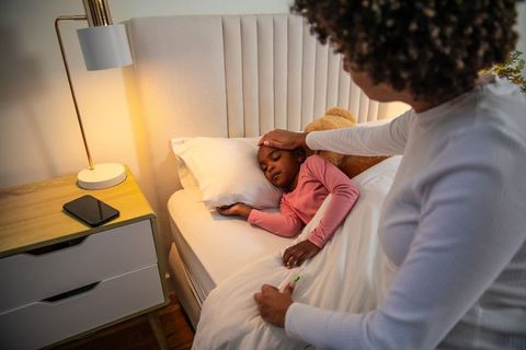 Caring mother checking sick child's temperature during bedtime