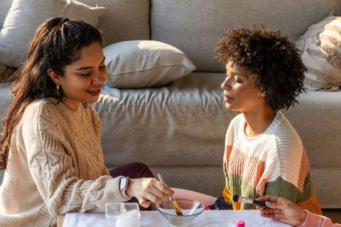 Diverse women mixing paint and crafting in cozy sunlit living room wearing knit sweaters