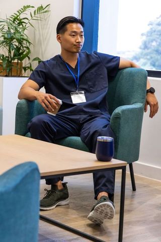 Relaxed asian healthcare worker taking break in modern clinic lounge wearing navy scrubs