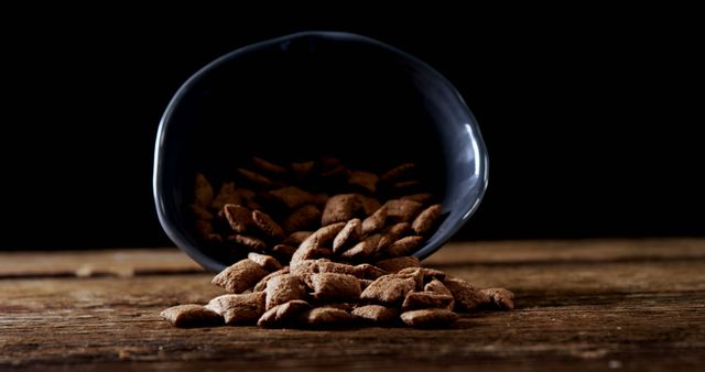 A bowl tipped over on a wooden surface, spilling out almonds with a dark background, with copy space. Almonds are a nutritious snack, and the image captures a sense of motion and accidental spillage.