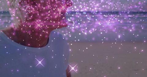 Senior woman on beach facing ocean at twilight with pink bokeh star flares dreamy overlay