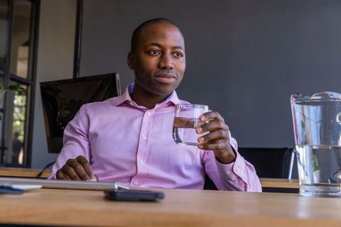 Businessman Drinking Water and Using Smartphone at Modern Office Table
