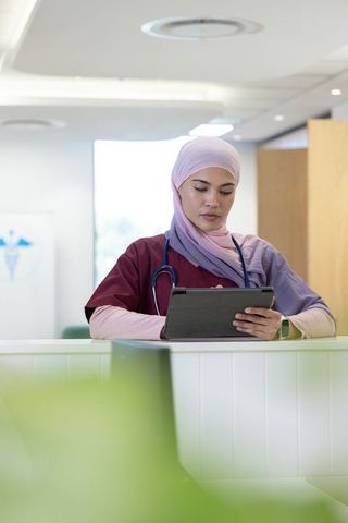 African nurse in hijab reviewing tablet at clinic reception desk, healthcare professional