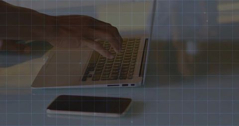 Hand typing on laptop keyboard with smartphone on table