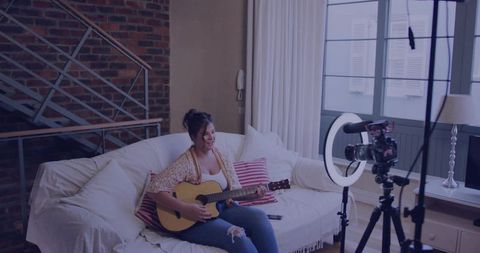 Woman Filming Guitar Performance in Cozy Living Room with Brick Wall