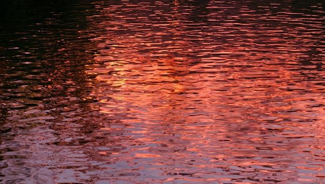 Sunset reflecting on rippling lake surface with warm orange and pink shimmer