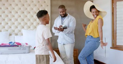African american family packing for vacation with checklist and playful mom in straw hat