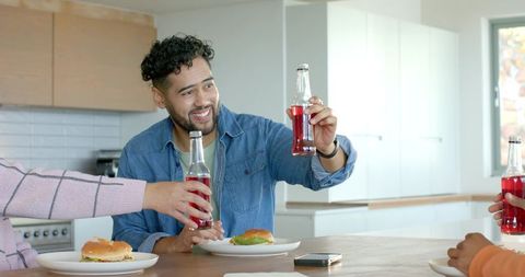Friends clinking glass bottles at kitchen island enjoying burgers and casual daytime gathering