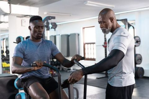 African american trainer coaching client on air bike, intense cardio and strength training