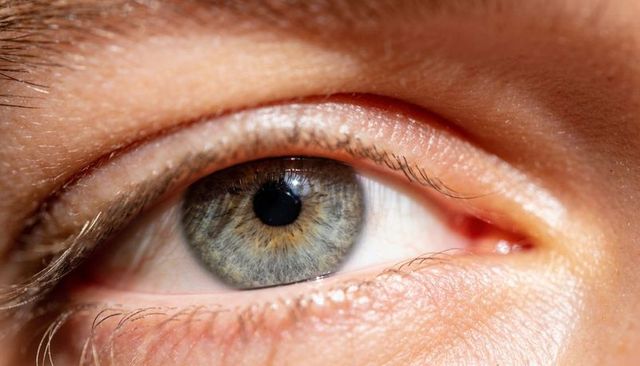 Macro close-up showing human eye with blue-gray iris, textured cornea, lashes and skin pores
