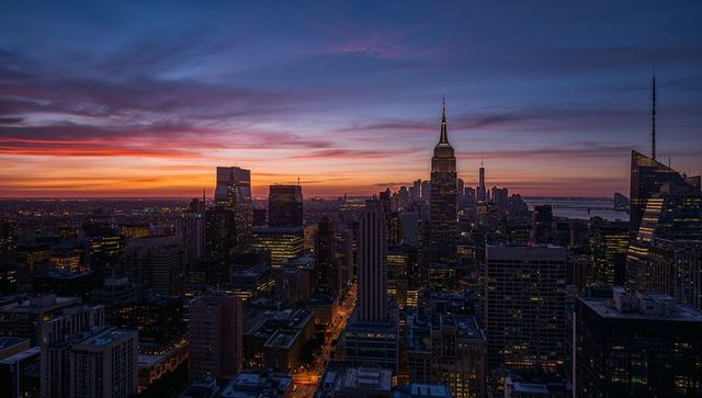 Glowing spire rising above Manhattan skyline at dusk with vibrant sunset and city lights