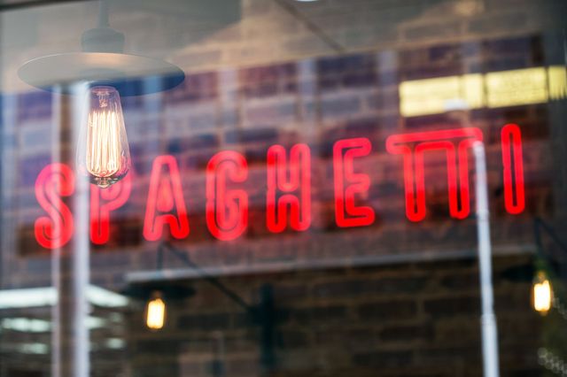 Neon 'Spaghetti' sign glowing through a restaurant window. Reflections and vintage lighting add ambiance. Perfect for illustrating Italian eateries, urban dining spots, vibrant city life, or promoting pasta-related content.