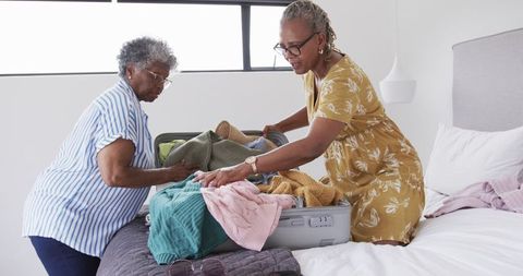 Senior female friends packing suitcase for vacation