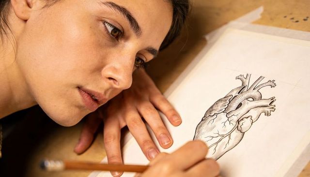 Young woman sketching detailed anatomical heart with pencil on masking-taped paper closeup