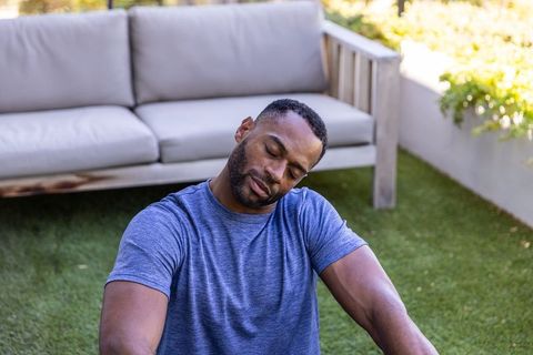 Mature african american man stretching neck on patio turf beside outdoor sofa