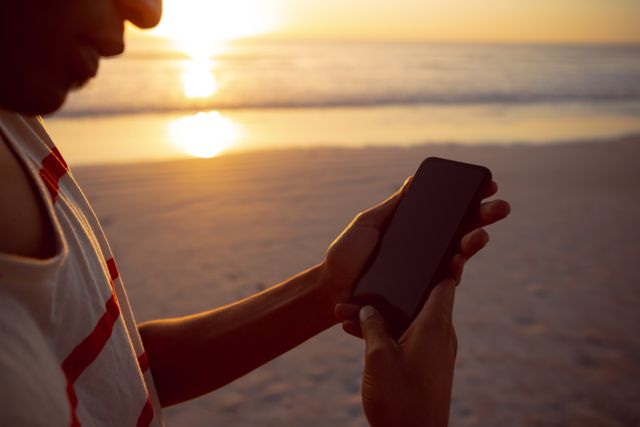 Mid section of man using mobile phone on the beach during sunset