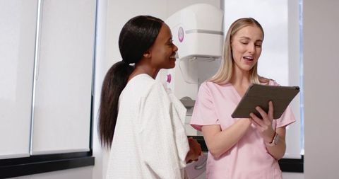 Radiology technologist explaining mammogram procedure holding tablet while patient smiling