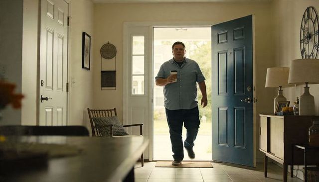Casual man entering home carrying coffee through open blue front door on sunny morning