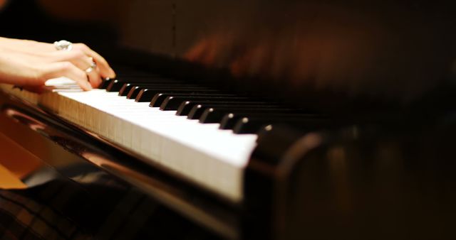 Close-up of hands playing grand piano keys under soft lighting. Ideal for illustrating concepts of music, performance, and artistic expression. Suitable for use in promotional materials for music schools, concert advertisements, and musical instrument stores.