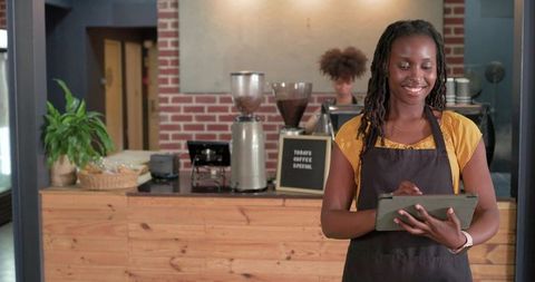 Smiling barista tapping tablet at rustic coffee counter with grinders pastries plant warm lighting