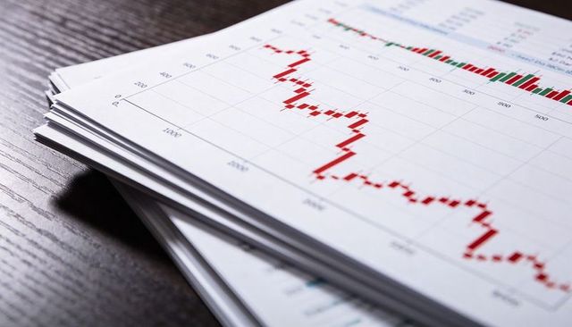 Stack of financial reports showing falling red candlestick chart on dark wood desk