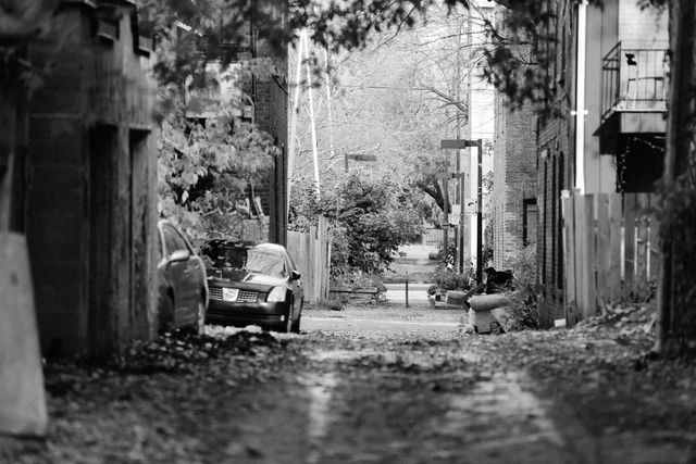 This black and white photograph depicts a desolate urban alley with an abandoned car. Fallen leaves are scattered on the ground and the alleyway seems empty and neglected. This image can be used to portray themes such as urban decay, loneliness, or nostalgia. Suitable for backgrounds, presentations, blog posts, or art projects emphasizing urban environments.