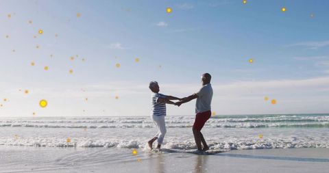 Mature couple holding hands spinning in shallow surf on sunny beach