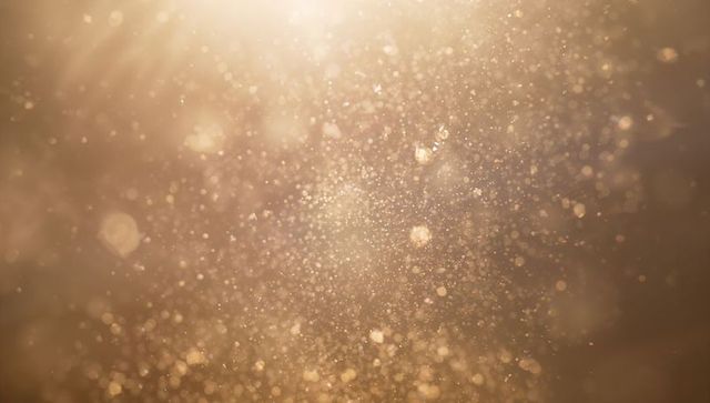 Glittering golden particles drifting through warm bokeh light for elegant backgrounds