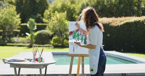 Senior woman painting outdoors near pool with art supplies