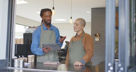Baristas discussing menu using tablet in modern coffeehouse with espresso machine