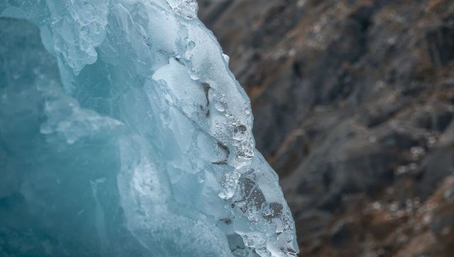 Turquoise glacier ice face melting on rocky mountain bedrock with droplets