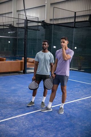 Two men standing on indoor padel court holding black paddles preparing to play