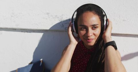 Young woman adjusting headphones against bright urban wall