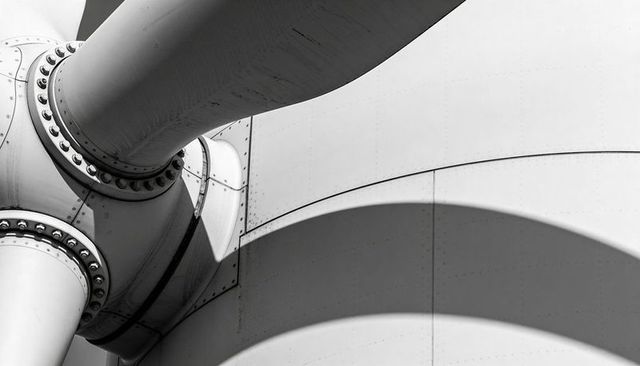 Wind turbine hub closeup showing blade root flange bolts rivets and curved shadow