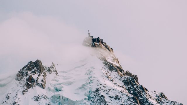 Snow-covered mountain peak with observatory nestled in fog creates feelings of serenity and awe. Ideal for travel blogs, outdoor adventure promotions, and nature scenery collections.
