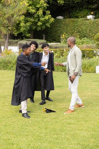 Smiling diverse male graduates greeting african american mentor on green campus lawn celebration