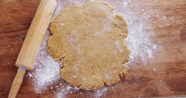 Rolling out cookie dough with a wooden rolling pin on a flour-dusted wooden surface is perfect for themes about home-cooking, baking, and kitchen activities. Great for use in culinary blogs, recipe websites, baking tutorials, and kitchen equipment advertisements.