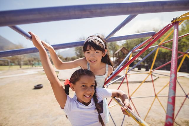 Two young girls enjoying their time on a playground climbing frame, smiling and having fun. Ideal for use in educational materials, advertisements for children's products, or articles about childhood development and outdoor activities.
