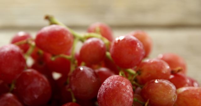 This image captures a close-up shot of fresh red grapes with water droplets, resting on a rustic wooden table. Ideal for use in healthy eating promotions, organic food advertisements, and natural ingredient marketing. Perfect for websites, blogs, or print materials focusing on nutrition, fruit-based recipes, or farm-to-table concepts.
